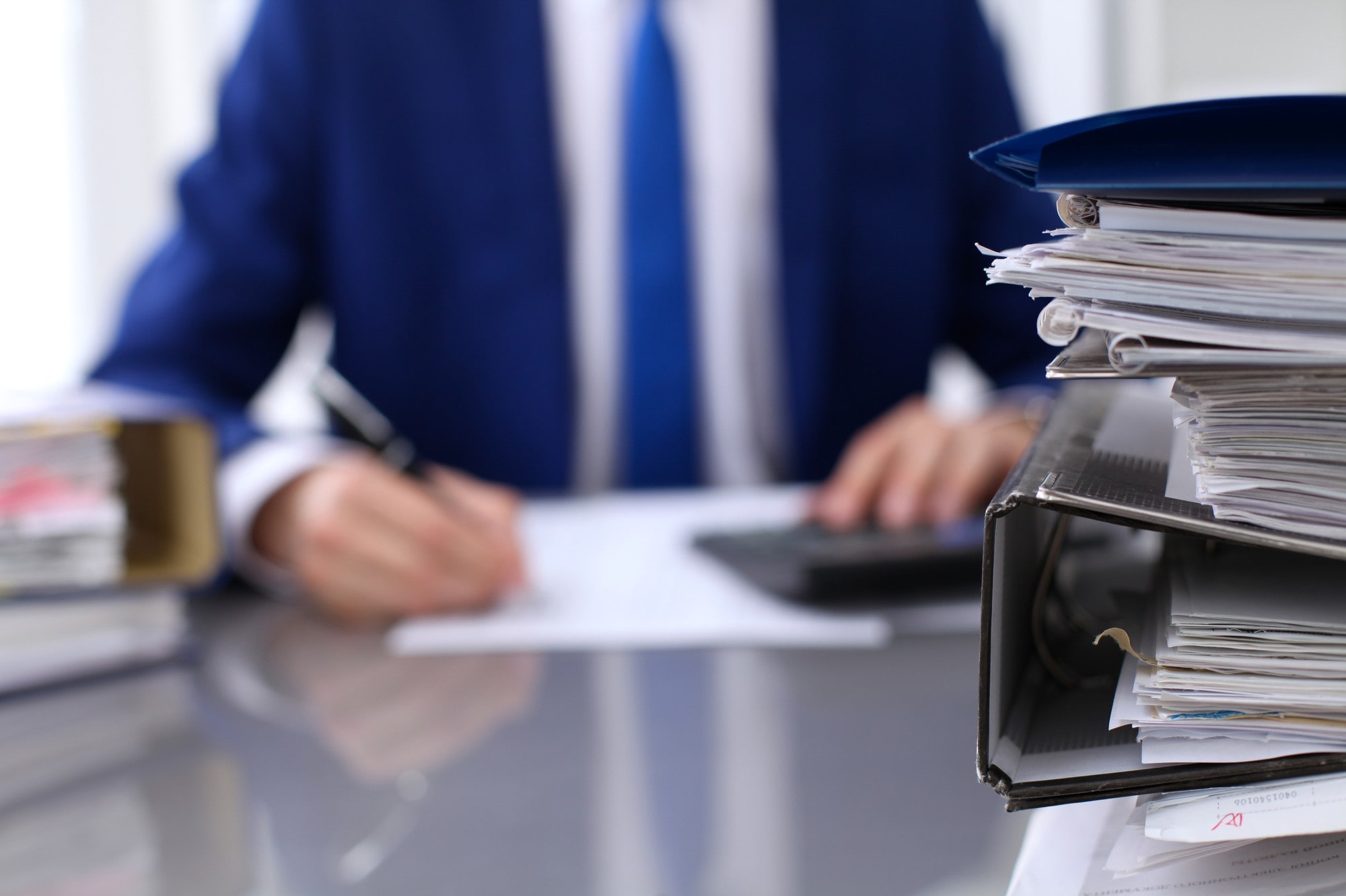 Suited man is seated at a desk, reviewing a stack of papers